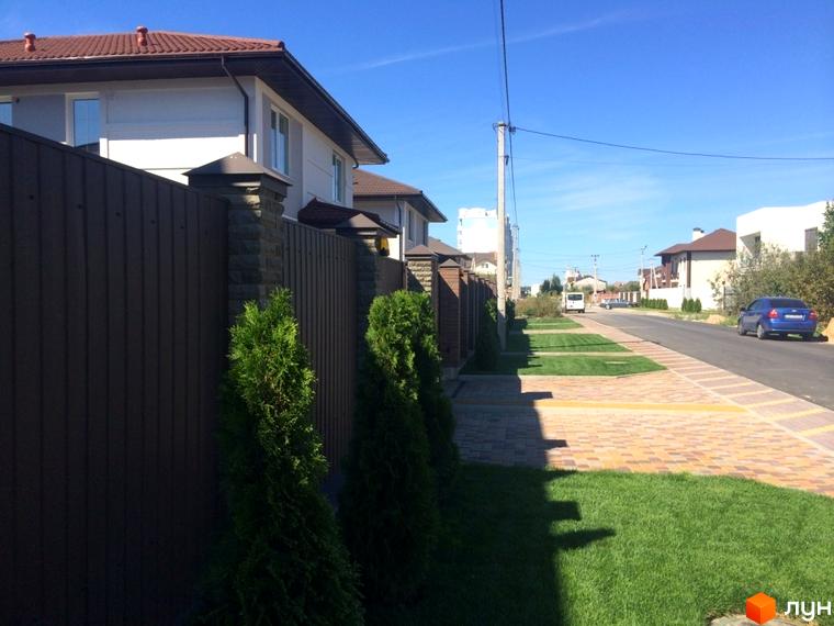 Будинки в котеджному містечку Петропавлівський Luxe з коричневими дахами та парканом. Зелені насадження та доглянута прибудинкова територія.