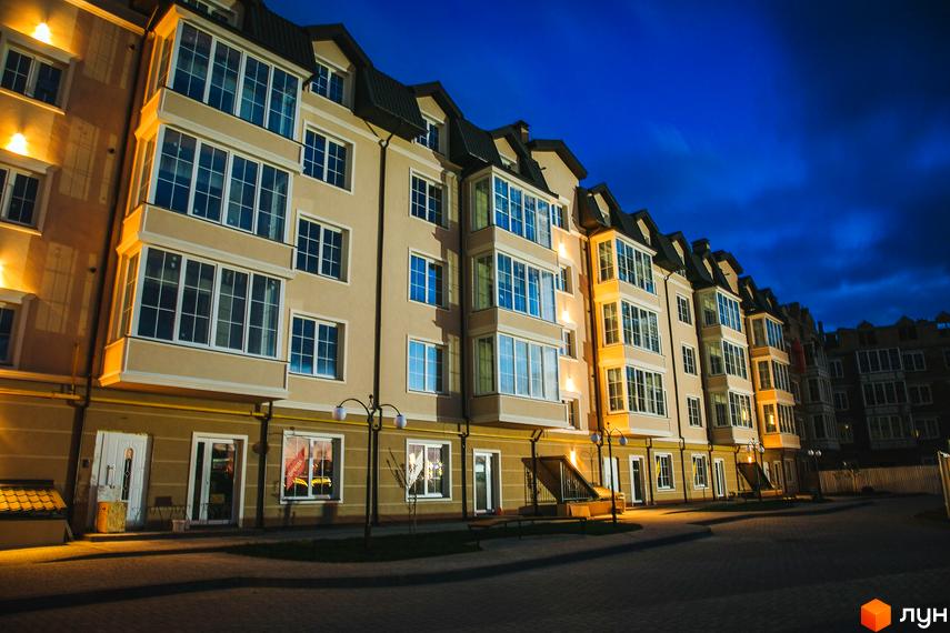 Житловий комплекс Маєток Боздош з великими вікнами та балконами, освітленням у вечірню пору. На передньому плані бруківка та ліхтарі.