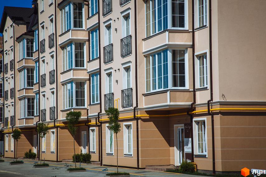 Житловий комплекс Маєток Боздош з фасадом у пісочних тонах, великими вікнами та кованими балконами. На прибудинковій території висаджені дерева, є тротуар.