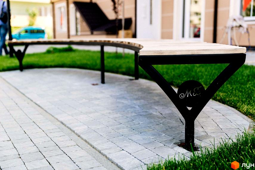 Житловий комплекс Маєток Боздош. Лавка з металевими опорами на території житлового комплексу, бруківка на доріжках та газон.