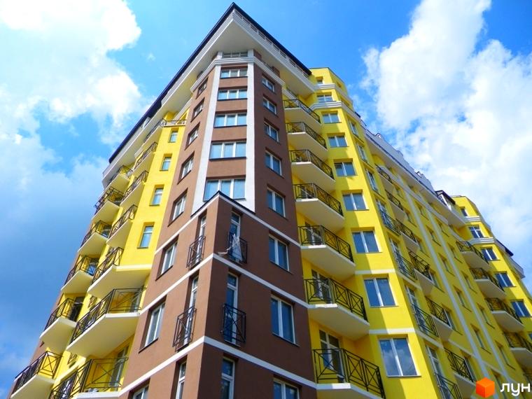 Житловий комплекс Велесгард: яскрава жовто-коричнева новобудова з балконами та блакитним небом. Зовнішній вигляд будівлі з безліччю вікон та лоджій.