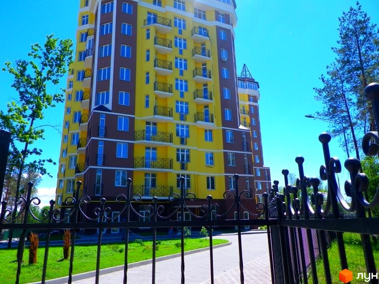 Житловий комплекс Велесгард: багатоповерховий будинок жовто-коричневого кольору з балконами під блакитним небом. Навколо зелений газон та огорожа.