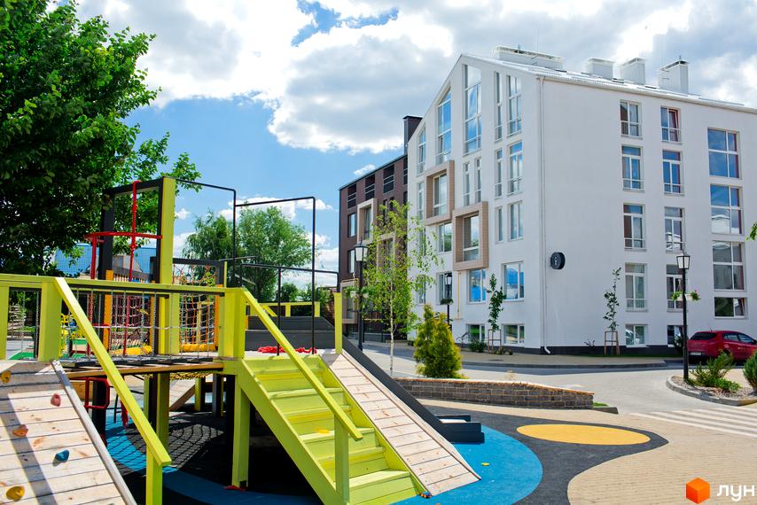 Житловий комплекс Білий Шоколад. Center. Зовнішній вигляд білої новобудови з великою кількістю вікон та дитячий майданчик поруч.