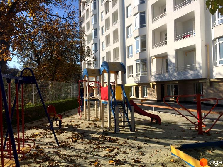 Житловий комплекс Kaiser з дитячим майданчиком та осінніми деревами. Сучасна новобудова з балконами та вікнами.