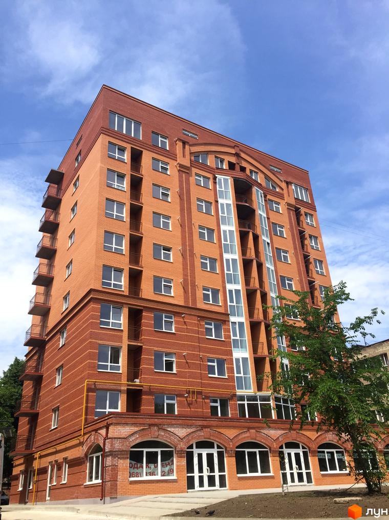 Фото фасаду цегляного будинку в Житловому районі Brooklyn. Багатоповерхівка з балконами та великими вікнами на фоні блакитного неба.