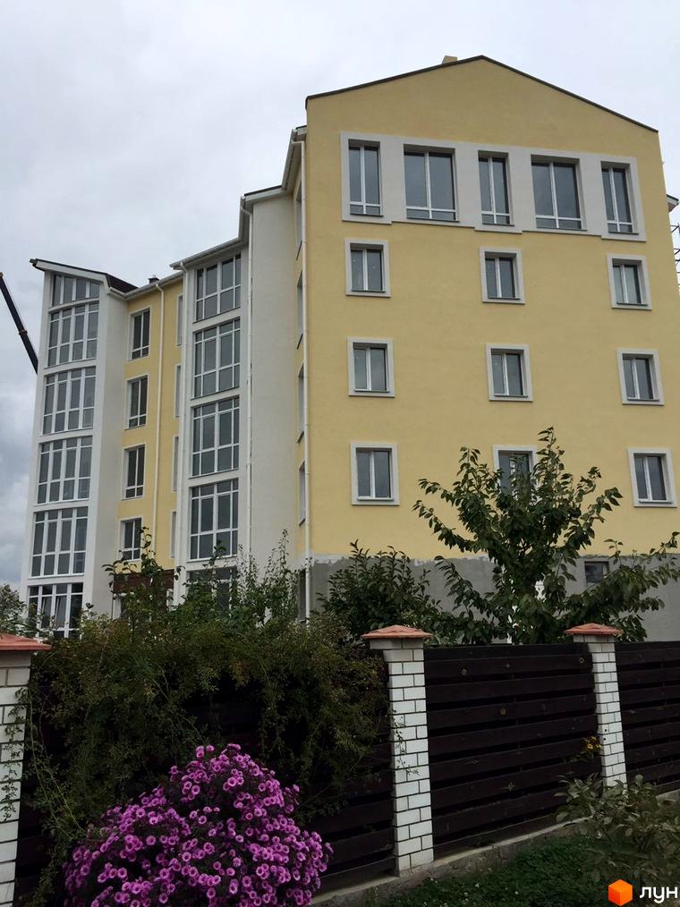 Зображення фасаду багатоповерхового будинку ЖК Мандарин. На передньому плані огорожа з рослинністю.