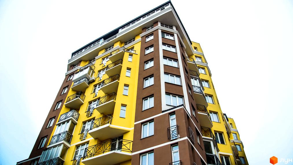 Житловий комплекс Велесгард: яскрава жовто-коричнева новобудова з балконами та великими вікнами. Зовнішній вигляд будинку з низького ракурсу.