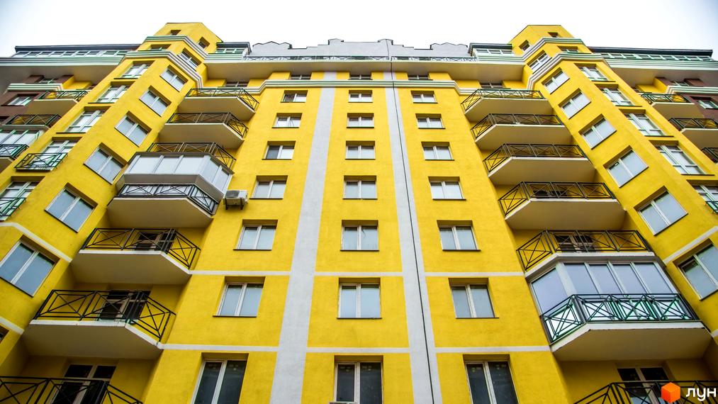 Яскрава жовта новобудова ЖК Велесгард з балконами та великими вікнами. Фасад будівлі прикрашений білими вертикальними смугами.
