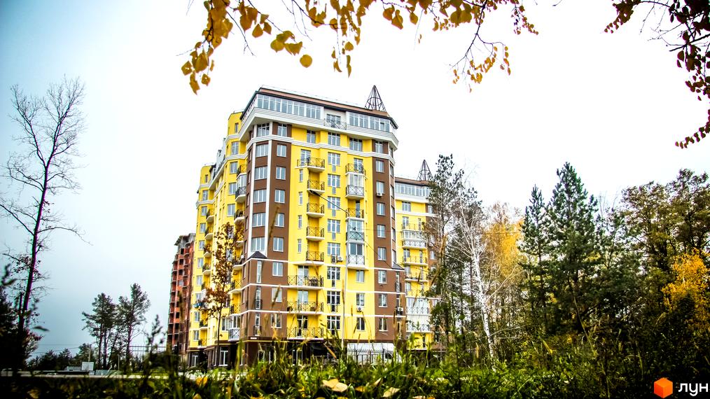 Житловий комплекс Велесгард: багатоповерховий будинок жовто-коричневого кольору з балконами та великими вікнами, оточений деревами восени.