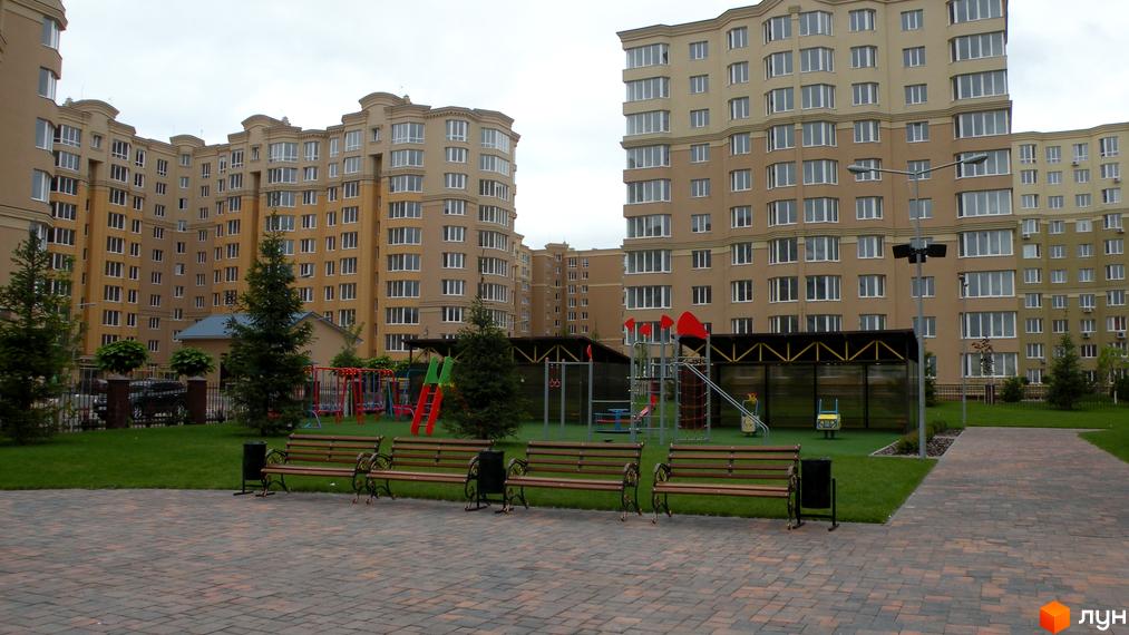 Житловий комплекс Софія Сіті з багатоповерховими будинками та дитячим майданчиком. Зелена зона з лавками та деревами.