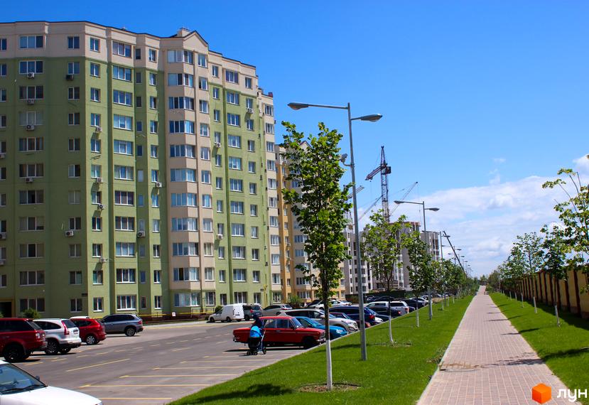 Житловий комплекс Софія Сіті з зеленим фасадом та світлими елементами. Прибудинкова територія з парковкою, алеями та деревами.