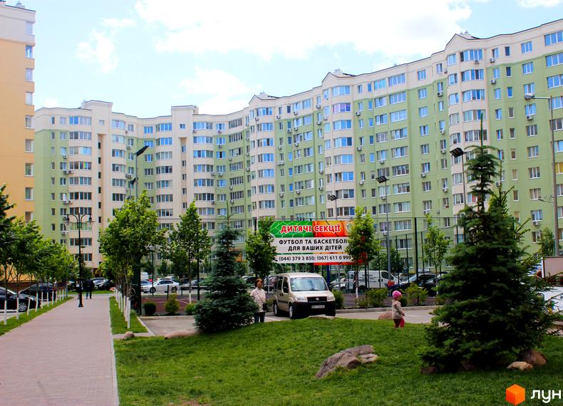 Житловий комплекс Софія Сіті з фасадами світло-зеленого та бежевого кольору. Прибудинкова територія з зеленими насадженнями, дитячим майданчиком та парковкою.