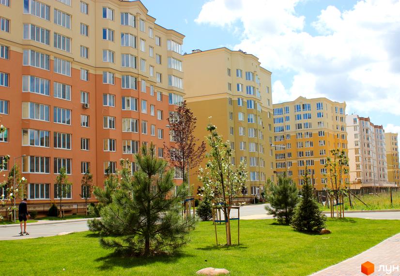 Житловий комплекс ЖК Софія Сіті. Багатоповерхові будинки з жовтою та помаранчевою обробкою фасаду, великою кількістю вікон. Прибудинкова територія з зеленим газоном та молодими деревами.