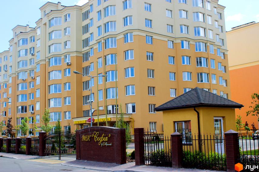 Житловий комплекс Софія Сіті з жовто-бежевим фасадом та великою кількістю вікон. Огороджена територія з кованими воротами та цегляними стовпами.