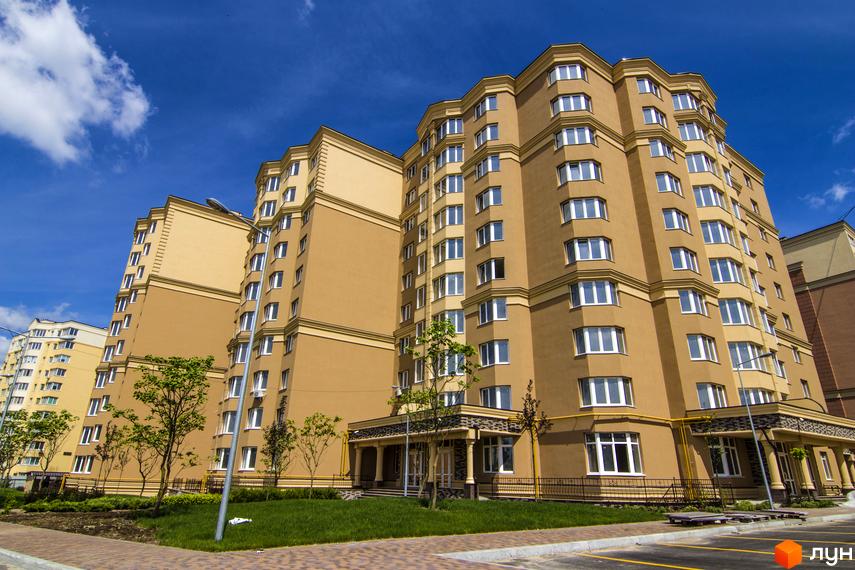 Зовнішній вигляд багатоквартирних будинків ЖК Софія Сіті з коричневим фасадом та білими вікнами. Прибудинкова територія з газоном та деревами.