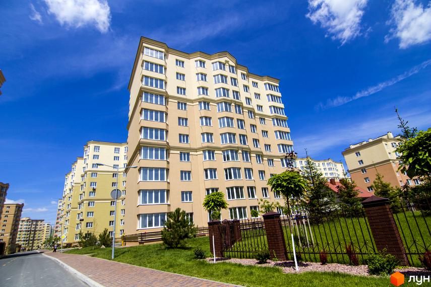 Житловий комплекс Софія Сіті. Багатоповерхові будинки світло-бежевого кольору з великими вікнами під блакитним небом. Прибудинкова територія з зеленим газоном та огорожею.