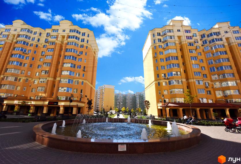 Житловий комплекс ЖК Софія Сіті з двома високими будинками жовтого кольору та фонтаном на прибудинковій території. Навколо будівель зелені насадження та місця для відпочинку.
