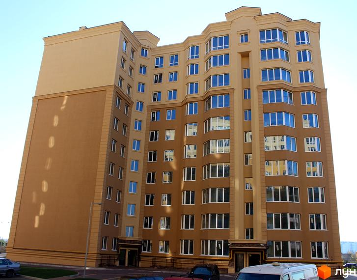 Зовнішній вигляд багатоповерхового будинку ЖК Софія Клубний з коричневими та бежевими фасадами та великою кількістю вікон. Навколо будинку видно прибудинкову територію та припарковані автомобілі.