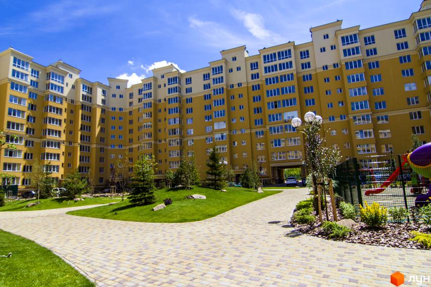 Житловий комплекс Софія Клубний: жовтий багатоповерховий будинок з синіми вікнами та доглянутою прибудинковою територією з дитячим майданчиком.