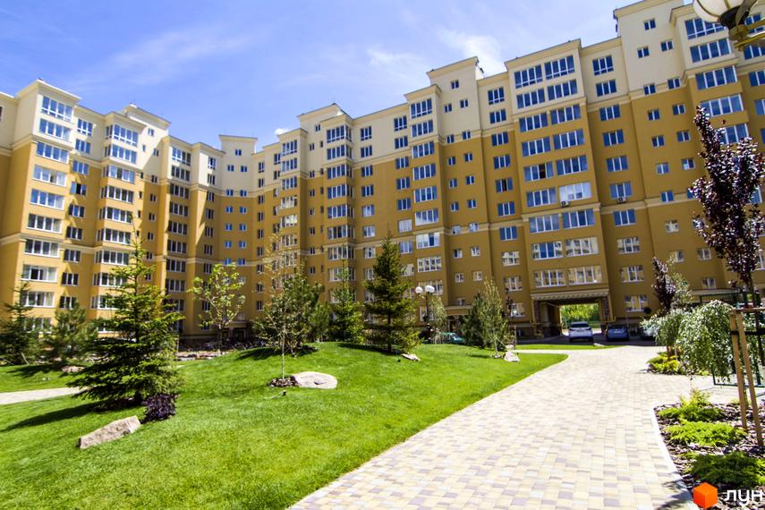 Житловий комплекс Софія Клубний: жовта багатоповерхівка з численними вікнами та доглянутою зеленою прибудинковою територією з доріжками та деревами.