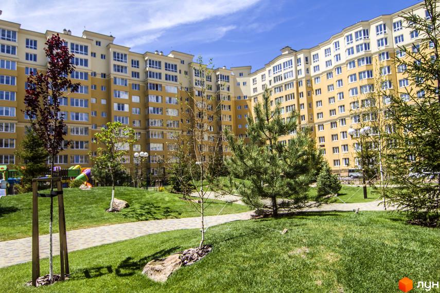 Житловий комплекс Софія Клубний. Великий жовтий будинок з багатьма вікнами та зеленою прибудинковою територією з деревами та дитячим майданчиком.