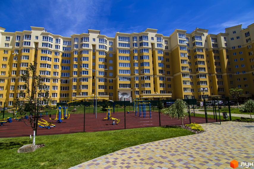 Житловий комплекс Софія Клубний: жовта багатоповерхівка з білими елементами фасаду та балконами. Поруч дитячий майданчик та зелена зона.