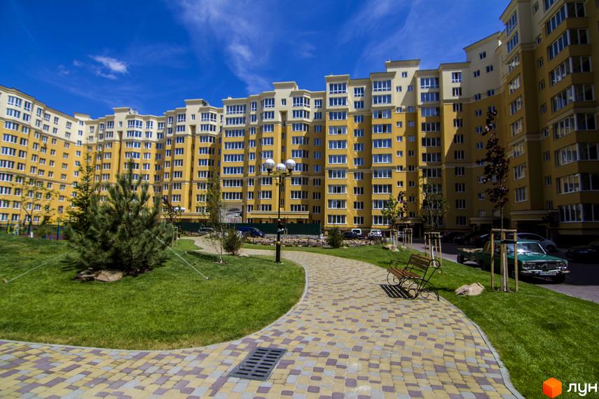 Житловий комплекс Софія Клубний: жовта багатоповерхівка з численними вікнами та балконами. Доглянута прибудинкова територія з газоном, доріжками та лавками.