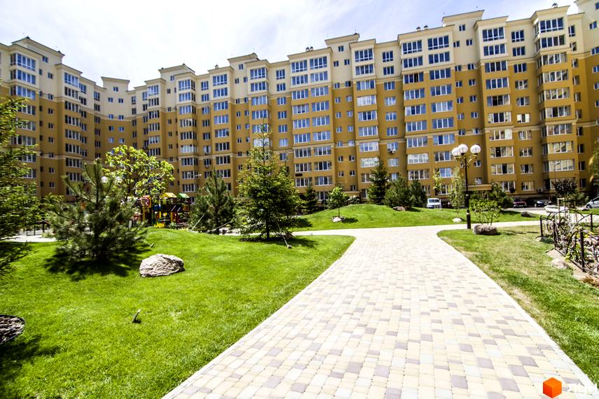 Житловий комплекс Софія Клубний. Зовнішній вигляд будівлі з жовтим фасадом та численними вікнами. Прибудинкова територія з доглянутим газоном, деревами та пішохідною доріжкою.