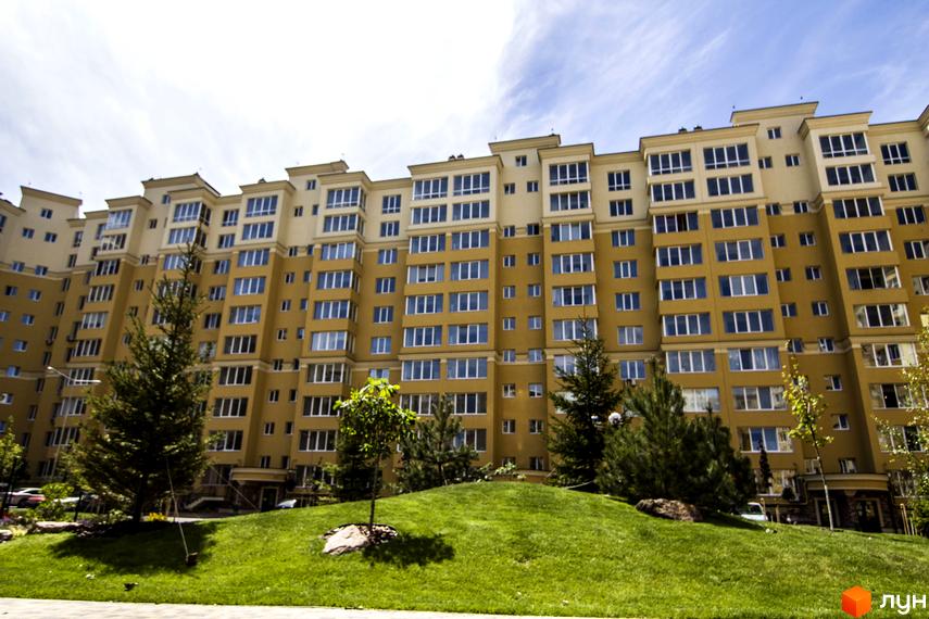 Фасад житлового комплексу Софія Клубний у жовтих тонах з великою кількістю вікон. На передньому плані зелений газон та дерева.