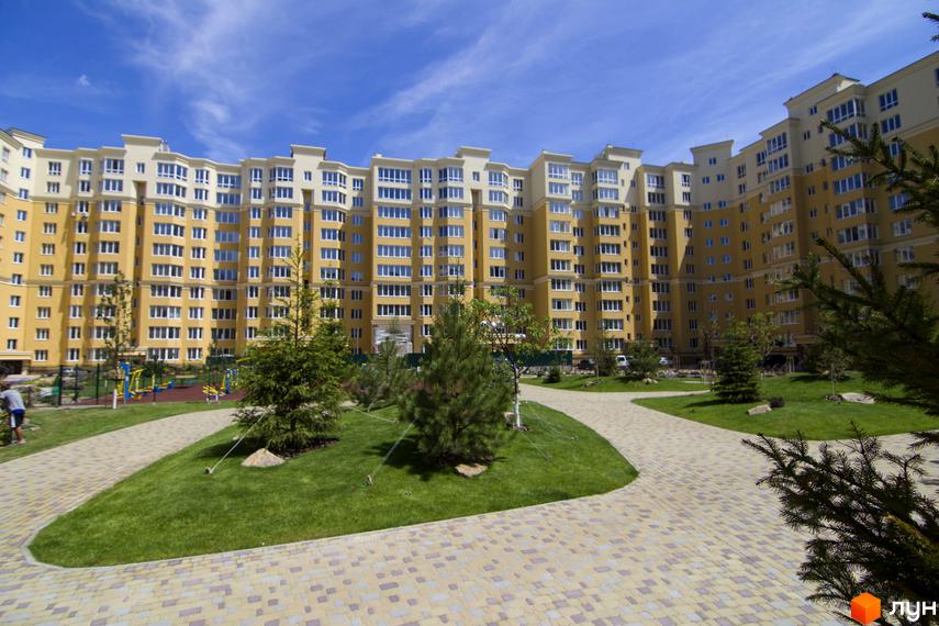 Житловий комплекс Софія Клубний - жовта багатоповерхівка з численними вікнами та балконами. Прибудинкова територія з зеленими газонами, деревами та пішохідними доріжками.