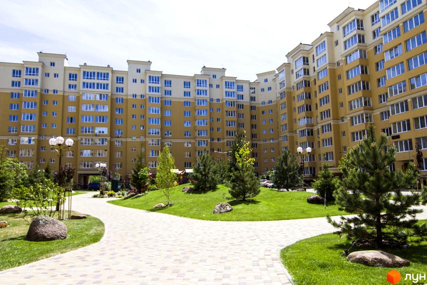 Житловий комплекс Софія Клубний - жовтий будинок з синіми вікнами та прибудинкова територія з зеленим газоном та доріжками.