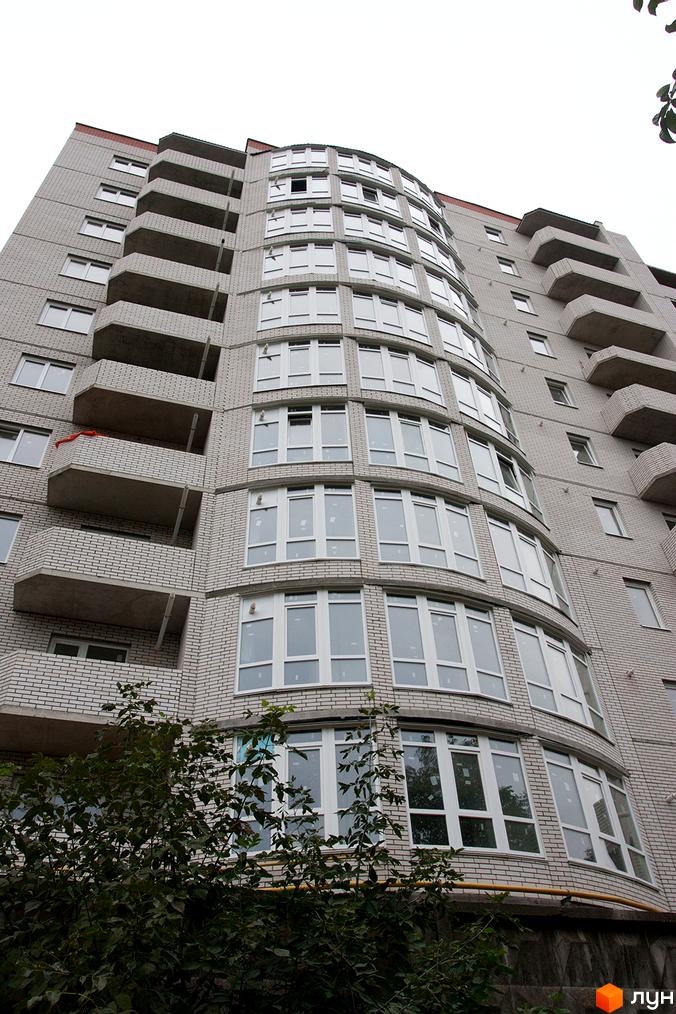 ЖБК Південно-Західний: багатоповерховий будинок з вигнутим фасадом зі світлої цегли та численними вікнами. На передньому плані зелені дерева.