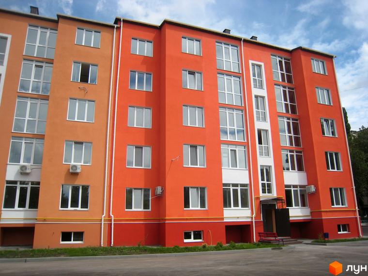 Зовнішній вигляд багатоповерхового житлового комплексу Уютний з яскравим фасадом та вікнами. Навколо будинку облаштована прибудинкова територія з лавкою та зеленню.