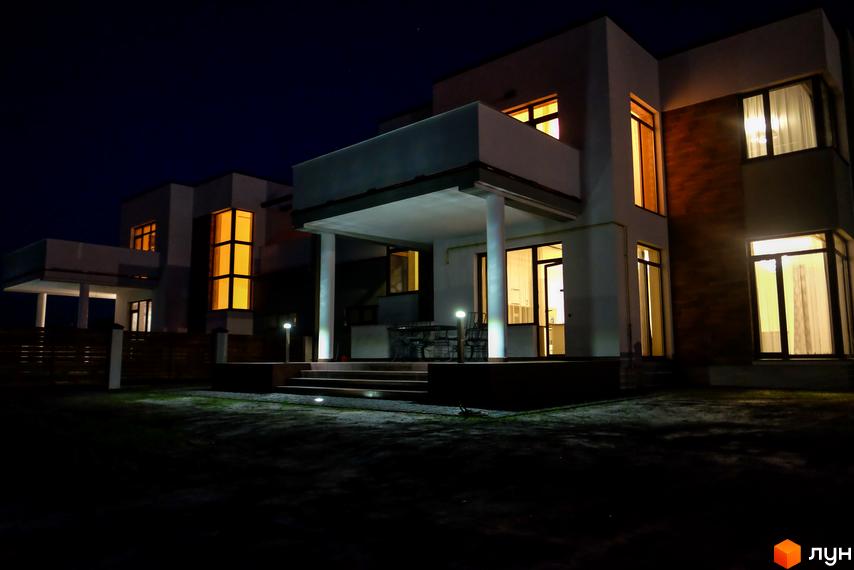 Котеджне містечко Riviera вночі. Сучасний двоповерховий будинок з великими вікнами та підсвіткою. Територія навколо будинку освітлена ліхтарями.