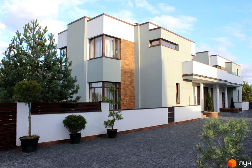 Котеджне містечко КМ Riviera. Фасад будинку виконаний у світлих тонах з дерев'яними вставками. Прибудинкова територія з доглянутими деревами та бруківкою.