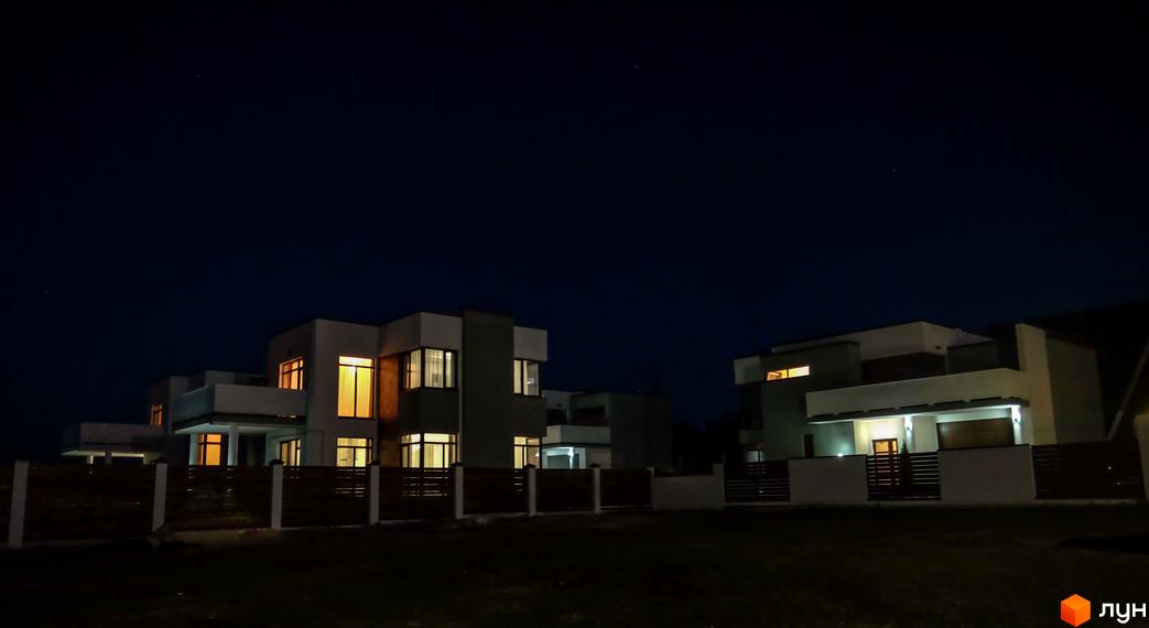 Нічний вигляд котеджного містечка КМ Riviera. Сучасні будинки з підсвіченими вікнами та огороджена територія.