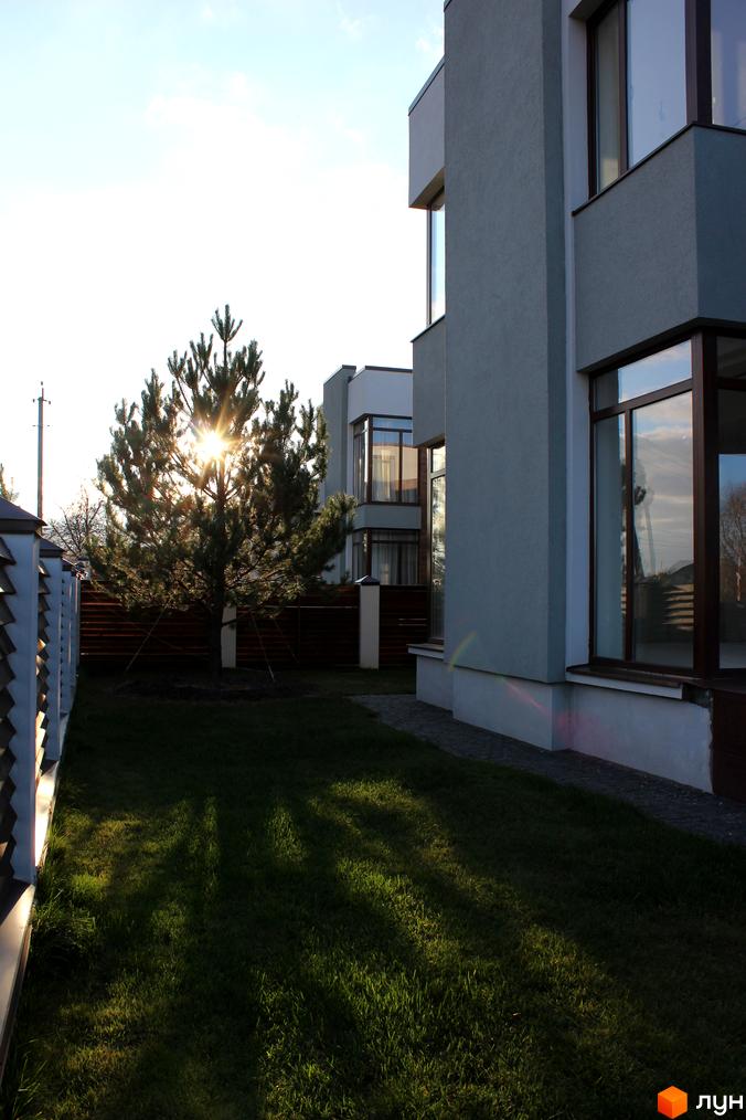 Котеджне містечко КМ Riviera: фасади будинків з великими вікнами та прибудинкова територія з деревами та газоном.