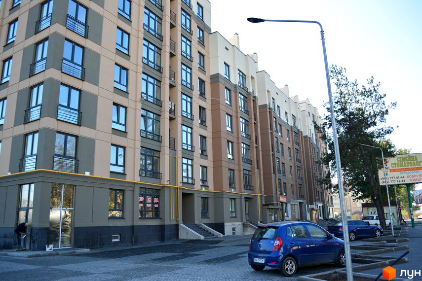 Житловий комплекс Барселона з бежево-сірими фасадами та численними вікнами. Перед будинком на бруківці припарковано синій автомобіль.