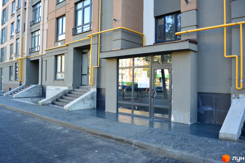 Зовнішній вигляд новобудови ЖК Барселона з входом та сходами. Фасад будинку сірого та коричневого кольору з жовтими комунікаціями.