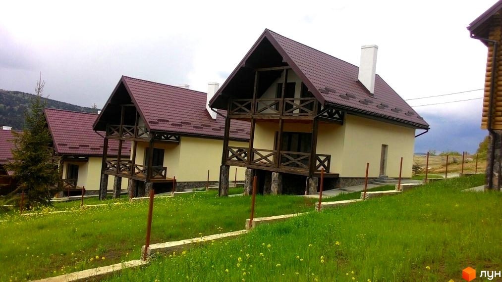 Новобудова на вулиці Грушевського, Київ. Триповерхові будинки з коричневими дахами та дерев'яними балконами розташовані на зеленій ділянці з квітами.