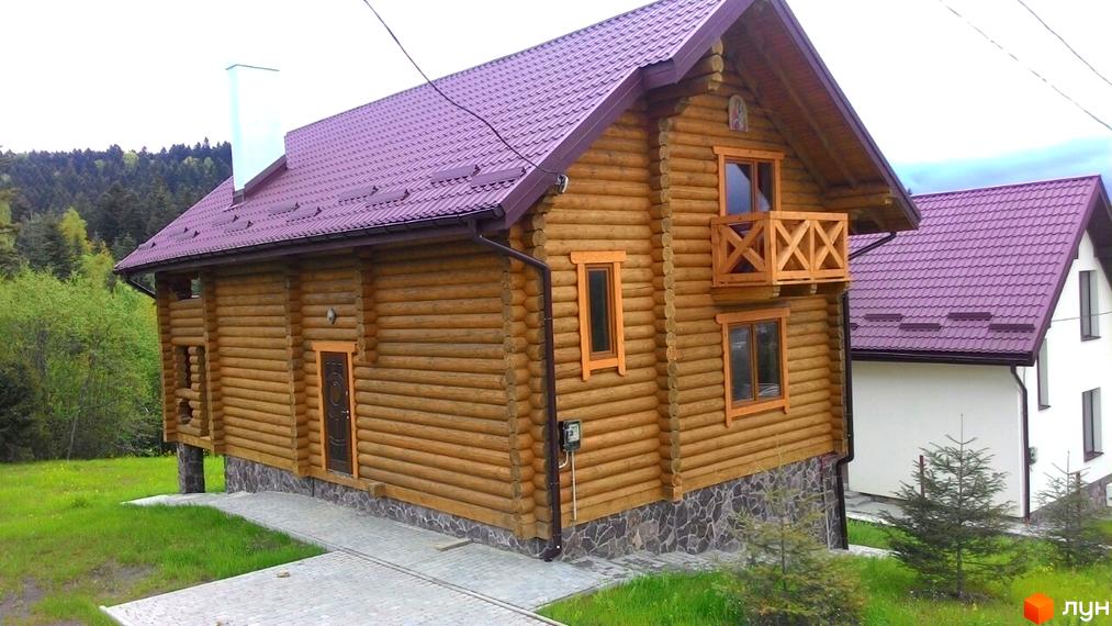 Двоповерховий дерев'яний будинок з фіолетовим дахом та балконом. Навколо будинку зелена галявина та дерева.