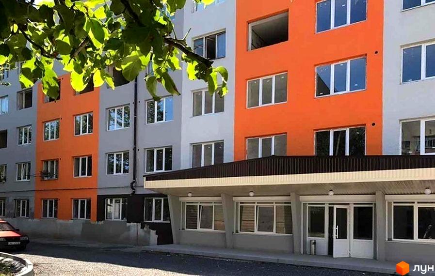 Зовнішній вигляд новобудови ЖК Мрія з яскравою оранжевою та сірою фасадною частиною. Навколо будівлі облаштована прибудинкова територія з дорогою та зеленими насадженнями.