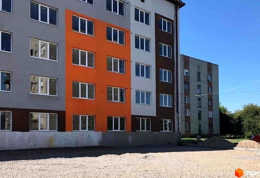 Зовнішній вигляд новобудови ЖК Мрія з яскравим фасадом та вікнами. Прибудинкова територія з гравієм та будівельними матеріалами.