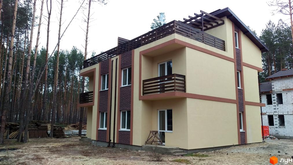 Зображення триповерхового будинку в Котеджному містечку Лісове-2. Вигляд фасаду з балконами та дерев'яною обробкою на тлі соснового лісу.