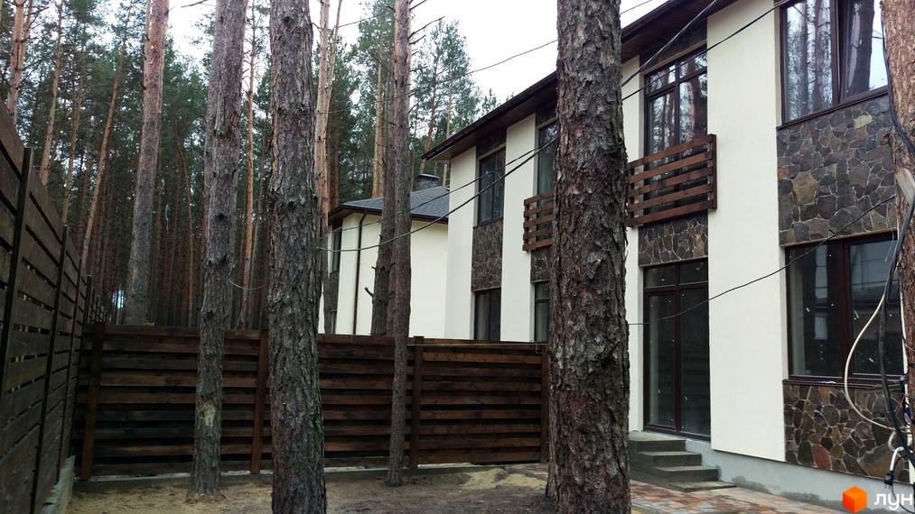 Зовнішній вигляд будинку КМ Лісове-3 з дерев'яним парканом та соснами навколо. Огляд новобудови та прибудинкової території.
