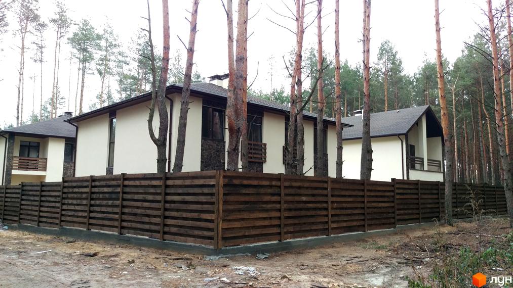 Котеджне містечко КМ Лісове-3: фасади будинків з темним дахом та дерев'яним парканом на фоні лісу. Прибудинкова територія з деревами та парканом.