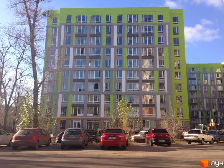 Новобудова ЖК Lemongrass з яскравим зеленим фасадом та сірими елементами. На прибудинковій території розташовані автомобілі та дерева.