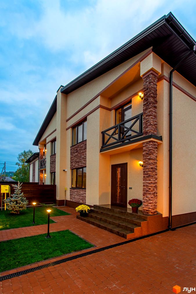 Котеджне містечко КМ Злагода: двоповерховий будинок з кам'яним оздобленням та балконом. Озеленена прибудинкова територія з ліхтарями та бруківкою.