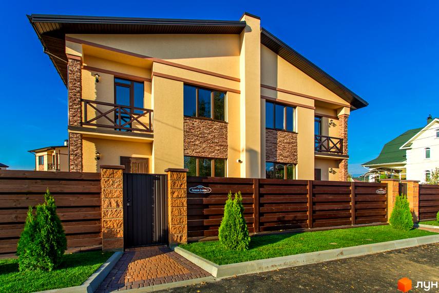 Котеджне містечко Злагода. Зовнішній вигляд двоповерхового будинку з коричневим парканом та зеленими туями. Новобудова з балконом та вікнами.