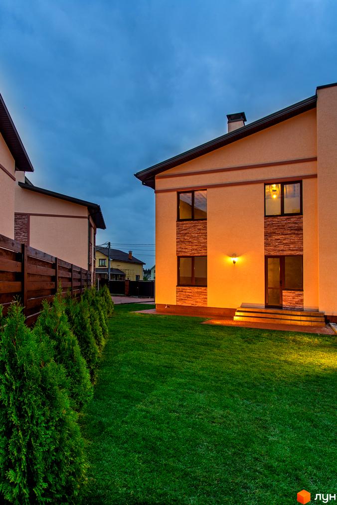 Будинок з бежевим фасадом та кам'яними вставками у Котеджному містечку Злагода. Доглянута прибудинкова територія з газоном та туями.